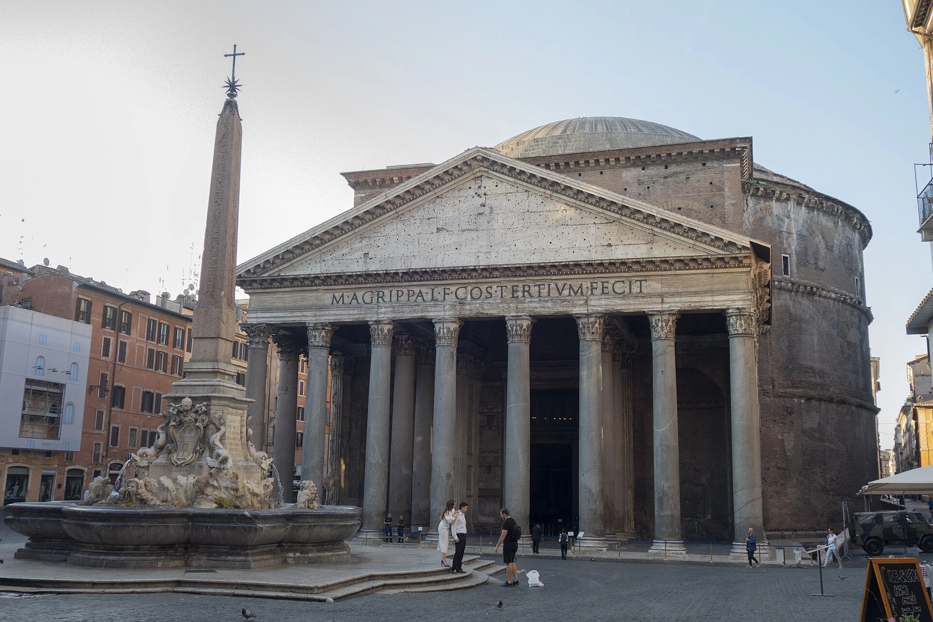 Fachada del Panteón con columnas, frontón e inscripción; un obelisco y una fuente delante.